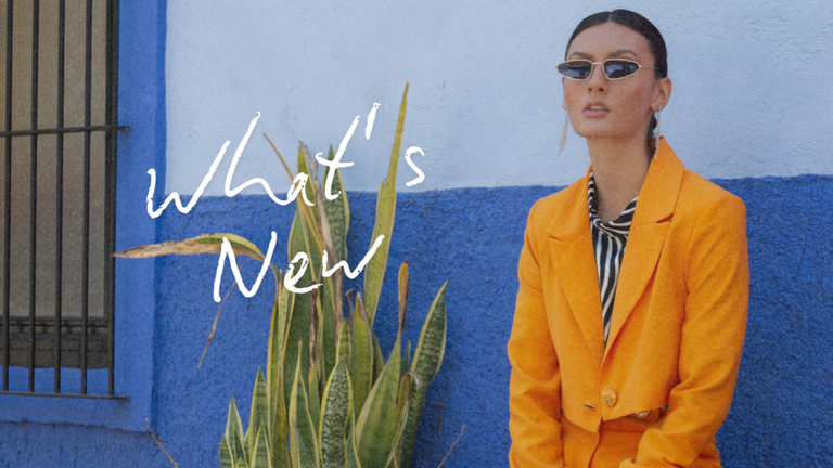 Person wearing an orange blazer in front of a blue wall with 'What's New' text.
